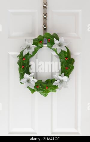 Porta natale Laurel con bacche rosse e fiori bianchi di poinettia su una porta bianca Foto Stock