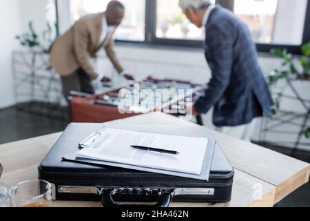 fuoco selettivo del contratto sulla valigetta vicino agli uomini d'affari anziani che giocano il calcio da tavolo su sfondo sfocato Foto Stock