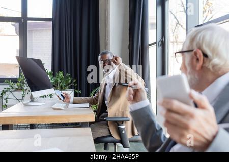 un uomo d'affari afro-americano che guarda un collega anziano offuscato mentre lavora in ufficio Foto Stock