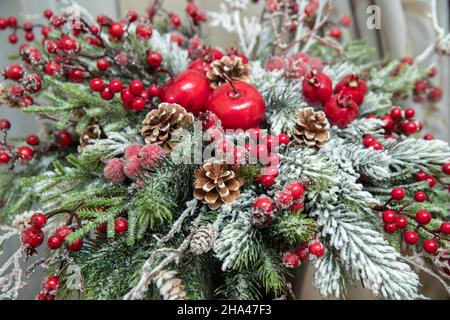 Bouquet invernale di rami di abete rosso innevato e coni con bacche rosse di rowan e mele, piccoli melograni Foto Stock