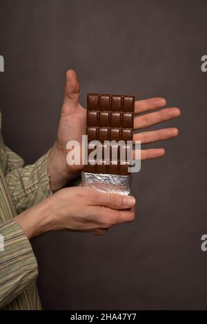 Uomo bianco che presenta una barra di cioccolato in camicia a righe su sfondo grigio Foto Stock