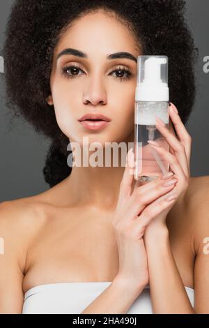 giovane afroamericana con pelle perfetta e trucco naturale tenendo schiuma detergente isolato sul grigio Foto Stock