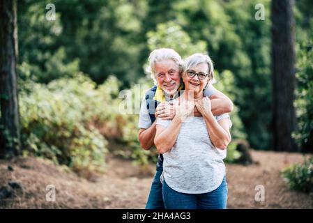 romantico amore felice coppia anziano godere abbraccio mentre in piedi nella foresta, sorridente marito abbracciare moglie da dietro ritratto di romantica età vecchia coppia trascorrere tempo libero a foresta Foto Stock