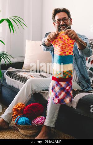 un uomo adulto felice mostra il suo lavoro colorato lavorato a maglia di lana fatto a casa in relax e tempo libero al coperto. goduto di uomini maturi in stile di vita femminile tradizionale attività Foto Stock