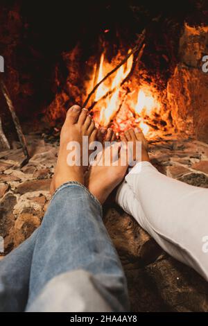 primo piano di coppia a piedi nudi godere l'amore e la relazione rilassante di fronte a un camino a casa. casa tempo libero o camera d'hotel concetto di stile di vita. amicizia persone in inverno Foto Stock