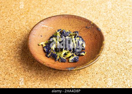 Lotto di clitoria ternatea secca intera in ciotola di ceramica sulla superficie di sughero Foto Stock