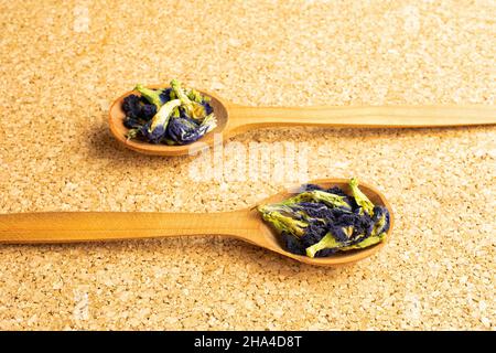 Lotto di clitoria ternatea secca intera in un cucchiaio di legno sulla superficie di sughero Foto Stock