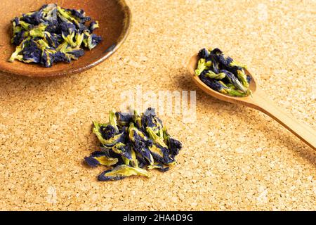 Lotto di clitoria ternatea secca intera in un cucchiaio di legno in ciotola di ceramica sulla superficie di sughero Foto Stock