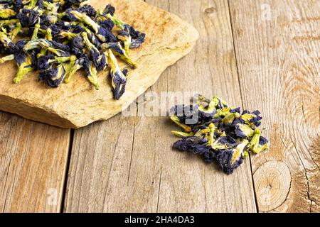 Lotto di clitoria ternatea secca intera con pietra piatta naturale su legno vecchio Foto Stock