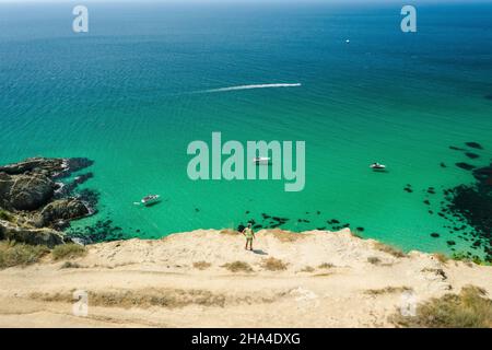 uomo viaggiatore sul bordo di fronte alla spiaggia bounty con mare azzurro cristallino in una giornata di sole. capo fiolent a sevastopol. vista aerea. Foto Stock
