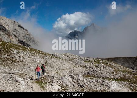 giovane coppia escursioni, discesa dal zugspitze, wetterstein montagne cielo blu, nuvole, umore nuvoloso, dietro di esso la cima di hochwanner 2744m, garmisch-partenkirchen, loisachtal, alta baviera, baviera, germania meridionale, germania, europa, Foto Stock