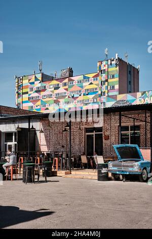 Un cortile con bar nel quartiere Hipster Leninsky vicino a via Oktyabrskaya con un edificio colorato sullo sfondo, Minsk B. Foto Stock