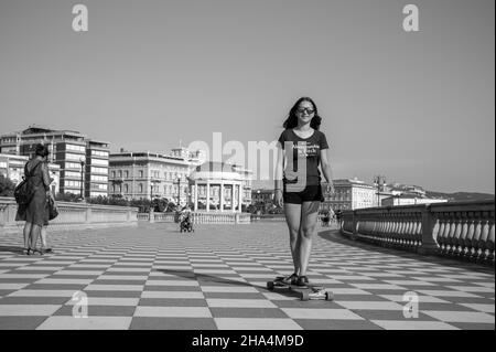 skater ragazza pattinare e saltare sulla terrazza mascagni a livorno, italia. il suo ampio belvedere sinuoso verso il mare con una superficie di pavimentazione di 8700 mq come una scacchiera e 4,100 balaustre Foto Stock