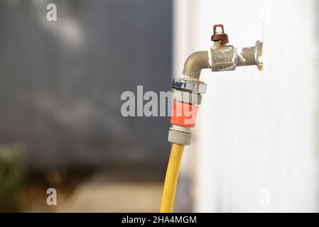 Un vecchio tubo da giardino è collegato in un vecchio rubinetto che sporge da una parete bianca, all'aperto Foto Stock