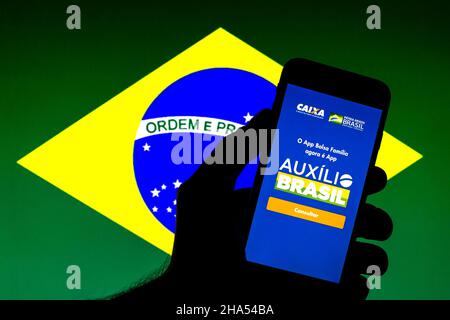 Barcellona, Catalogna, Spagna. 9th Dic 2021. In questa foto è mostrata un'app Auxilio Brasil visualizzata su uno smartphone con una bandiera del Brasile sullo sfondo. (Credit Image: © Thiago Prudencio/DAX via ZUMA Press Wire) Foto Stock