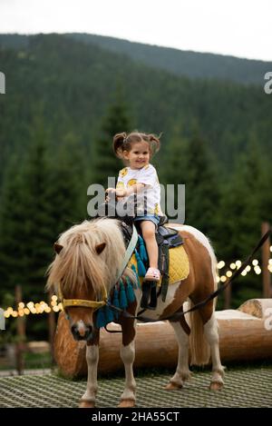 Bella emozione ragazza bambino a cavallo di un pony e sorridente. Foto Stock