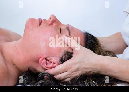 Massaggiatore femminile che fa un massaggio alla mano sul viso di un'altra donna. Massaggio energetico o reiki Foto Stock