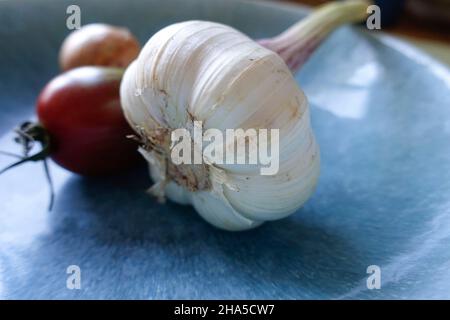 bulbo d'aglio su un piatto blu. ci sono verdure sullo sfondo. Foto Stock
