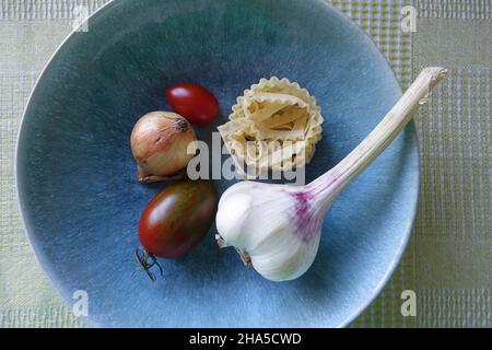 aglio, verdure e pasta sono in un piatto blu. ingredienti per un delizioso piatto di pasta. Foto Stock