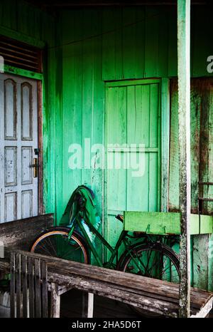 Una bicicletta verde si appoggia contro una casa dipinta di verde a Palangkaraya, Kalimantan centrale, Borneo Indonesia. Foto Stock