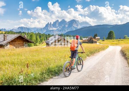 ciclista in e-bike tra le capanne della fuciade con la pallida catena montuosa di san martino sullo sfondo, comune di soraga,trento,trentino,italia Foto Stock