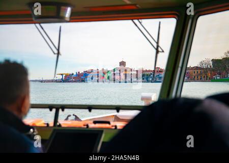 Venezia. Italia. L'isola di Burano con le sue case colorate è visibile dall'interno di un pozzetto di un traghetto con il capitano che la pilota. Vaporetto Foto Stock