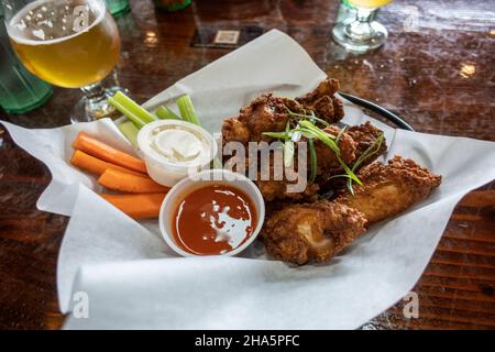 Primo piano di ali di pollo dorate e fritte in un cestino, accanto a tazze di ranch e salsa calda Foto Stock