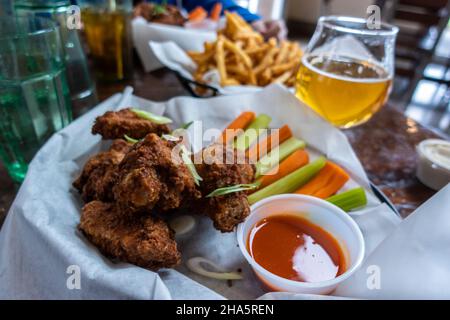Primo piano di ali di pollo dorate e fritte in un cestino, accanto a tazze di ranch e salsa calda Foto Stock