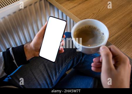 Smartphone con mano e bitcoin dorato, immagine mockup di un uomo che tiene il cellulare con schermo bianco vuoto mentre si siede in un caffè. Foto Stock