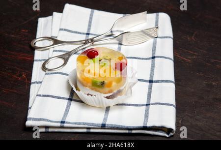 Torta con gelatina, kiwi, ciliegie e mango sul tavolo. Mini dessert yummy su sfondo di legno, primo piano. Foto Stock