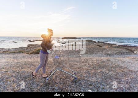 quanto consumo può tollerare la natura? donna con carrello vicino al mare Foto Stock