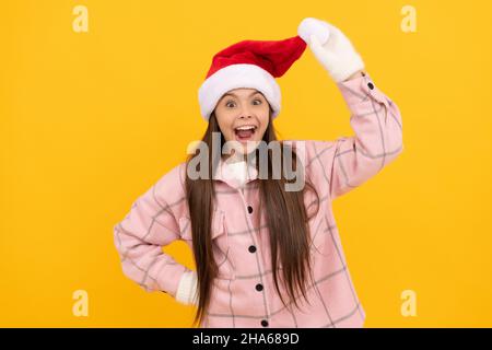 stupito bambino in cappello babbo natale e guanti invernali su sfondo giallo, dicembre Foto Stock