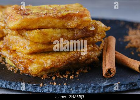 Delizioso dessert fatto in casa a Leche Frita con bastoncini di cannella e zucchero di canna su piatto di ardesia nera. Cucina tradizionale spagnola dolce. Foto Stock