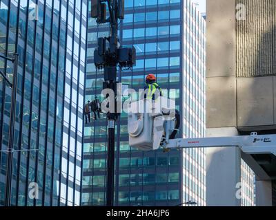 Tecnico che esegue la manutenzione delle antenne cellulari sul polo luminoso. Chicago, Illinois. Foto Stock