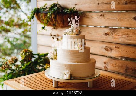 Torta nuziale bianca a tre piani con fiori su un tavolo di legno Foto Stock