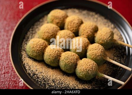 Gnocchi di mugwort ricoperti di farina di soia, serviti su un piatto nero posto su un vassoio rosso gnocchi giapponesi. Foto Stock