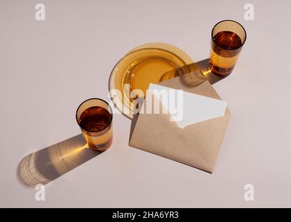 Mockup di cancelleria per matrimoni estivi. Sfondo beige con biglietti d'auguri semplici, inviti e vetro ambrato. Luce naturale e sovrapposizione d'ombra. Foto Stock