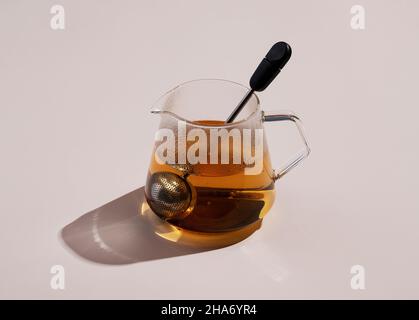 Tè e un filtro del tè in un contenitore di vetro su sfondo beige Foto Stock