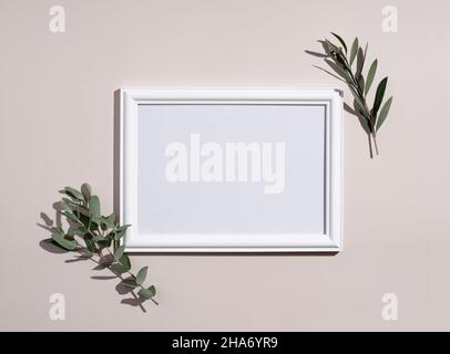 Cornice mockup con cornice in legno bianco. Foglie di eucalipto su sfondo beige. Luce naturale e sovrapposizione d'ombra. Disposizione piatta, vista dall'alto. Foto Stock