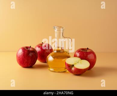 Aceto di mele in un contenitore di vetro su sfondo beige con un sacco di mele intorno. Foto Stock