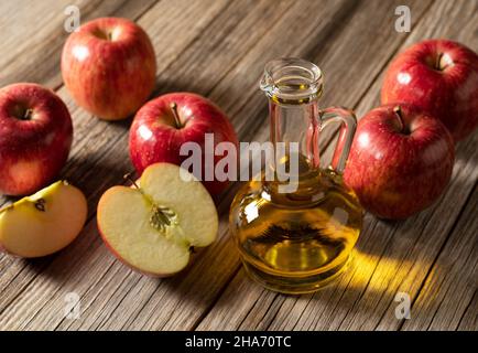 Aceto di mele in un contenitore di vetro su un fondo di legno con un sacco di mele intorno. Foto Stock