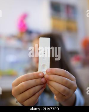 Profondità di campo poco profonda (fuoco selettivo) dettagli con le mani di una ragazza di 6 anni che tiene un test rapido antigene COVID-19, con un risultato negativo. Foto Stock