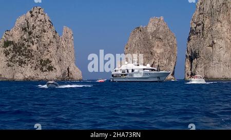 Le barche che passano tra la formazione rocciosa conosciuta come Faraglioni de mezzo, appena fuori dall'Isola di Capri, Italia, sono considerate la vista più iconica dell'isola. È una tradizione che baciare un partner sotto l'arco mentre una barca passa attraverso di essa porta buona fortuna alla coppia interessata. La nave al centro è il noleggio di barche a motore IDOL, Foto Stock