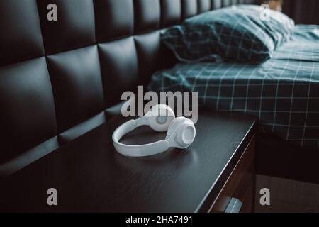 Le cuffie wireless bianche si trovano sul comodino in camera da letto, minimalismo negli interni. Foto Stock