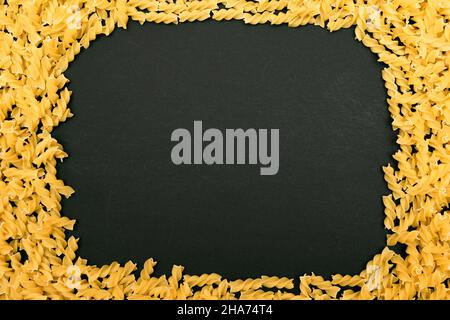 Una cornice in Fusilli Pasta non cotta frantumata sul tavolo Nero - Mock Up. Macaroni crudi e secchi. Cibo malsano e grasso. Cultura Italiana Foto Stock