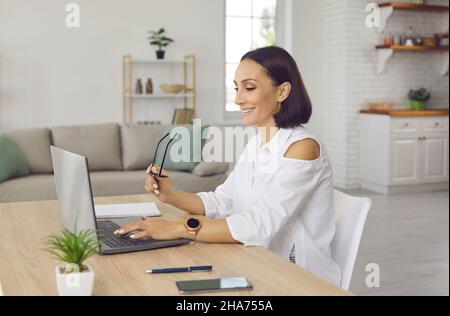 Una donna d'affari sorridente di mezza età lavora online su un notebook Foto Stock