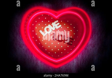 Confezione regalo a forma di cuore e scatola centrale a due testi 'LOVE' con doppio neon magico a forma di cuore o linee di luce fluorescente su sfondo scuro per un San Valentino Foto Stock