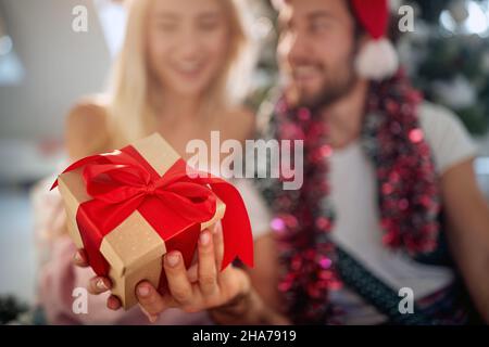 Primo piano di un regalo di natale tenuto da una giovane coppia che sta trascorrendo il tempo meraviglioso insieme in un'atmosfera festosa a casa. Natale, casa, relat Foto Stock