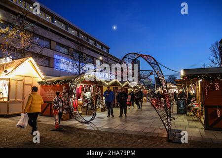 Le luci di Natale aggiungono un calore alle piccole bancarelle di legno al mercatino di Natale di Plymouth, le maschere mostrano che Covid è circa. Foto Stock