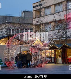 Le luci di Natale aggiungono un calore alle piccole bancarelle di legno del mercatino di Natale di Plymouth, dove un arco a forma di baule illuminato fornisce un grande set Foto Stock